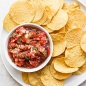 Tortilla chips on a large white plate surrounding a small dish of blender salsa.