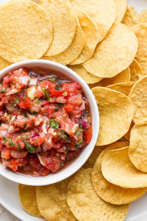 Tortilla chips on a large white plate surrounding a small dish of blender salsa.