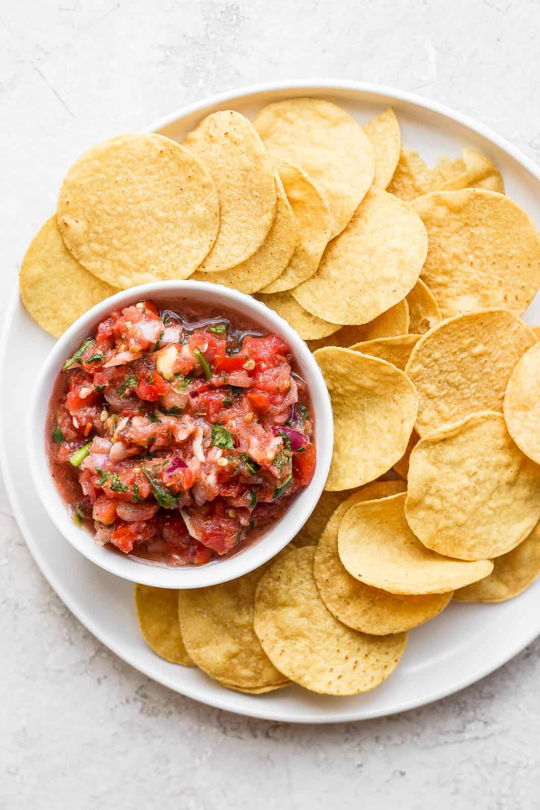 A plate of chips with a bowl of blender salsa. 