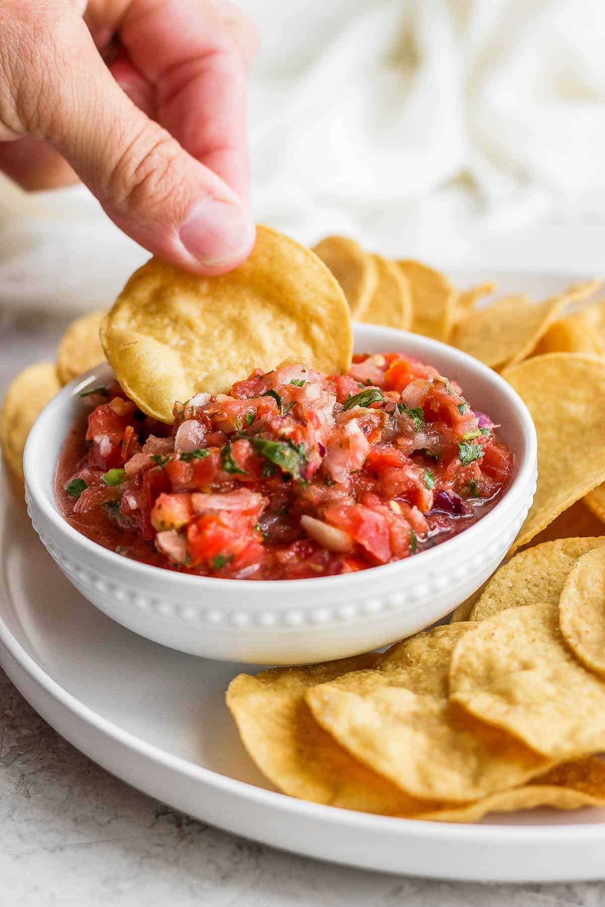 Someone dipping a chip into some salsa.