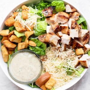 A large chicken caesar salad with a small bowl of caesar dressing.