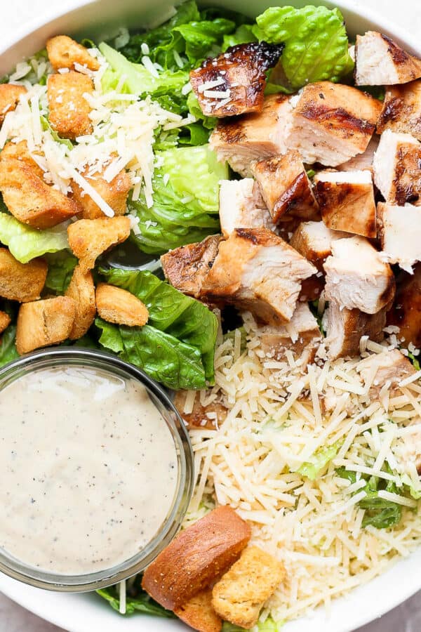 A large chicken caesar salad with a small bowl of caesar dressing.