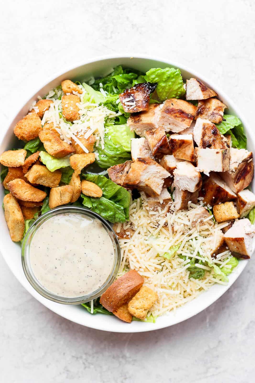 A bowl of grilled chicken caesar salad with a small dish of dressing.