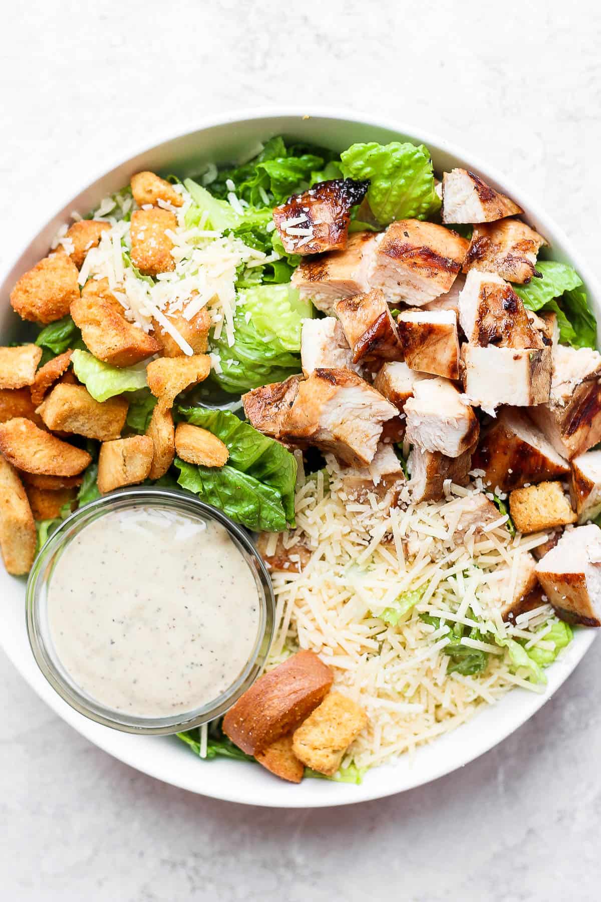 Grilled chicken caesar salad with a small dish of caesar dressing.
