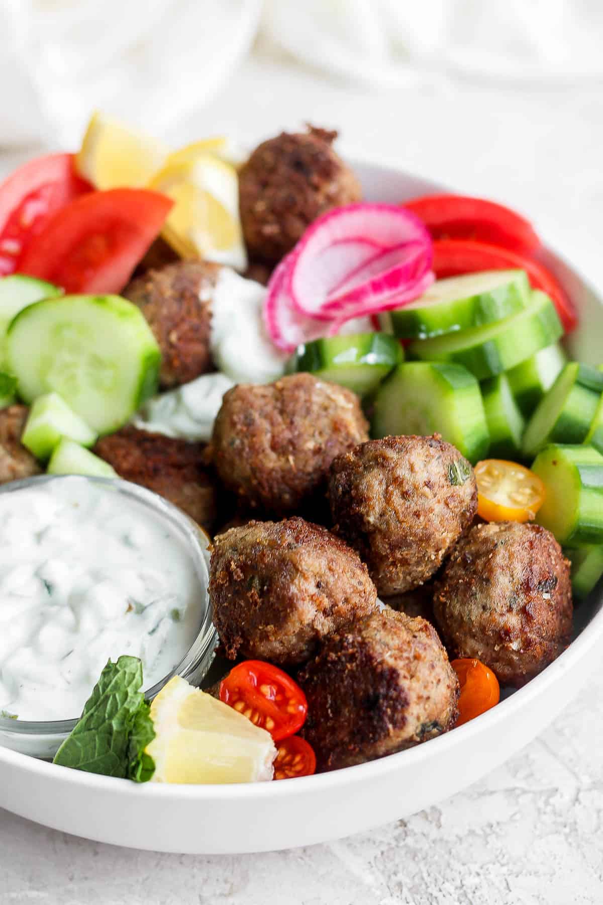 A gyro bowl with lamb meatballs, tzatziki sauce, tomatoes and cucumbers. 