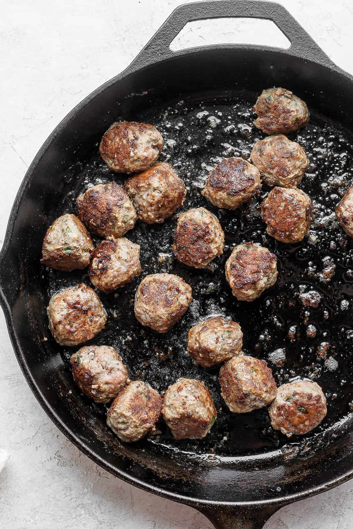 A cast iron skillet with lamb meatballs cooking inside. 