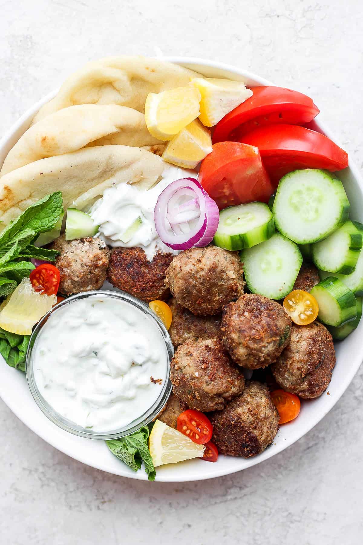 A gyro bowl with lamb meatballs, tzatziki sauce, tomatoes and cucumbers. 