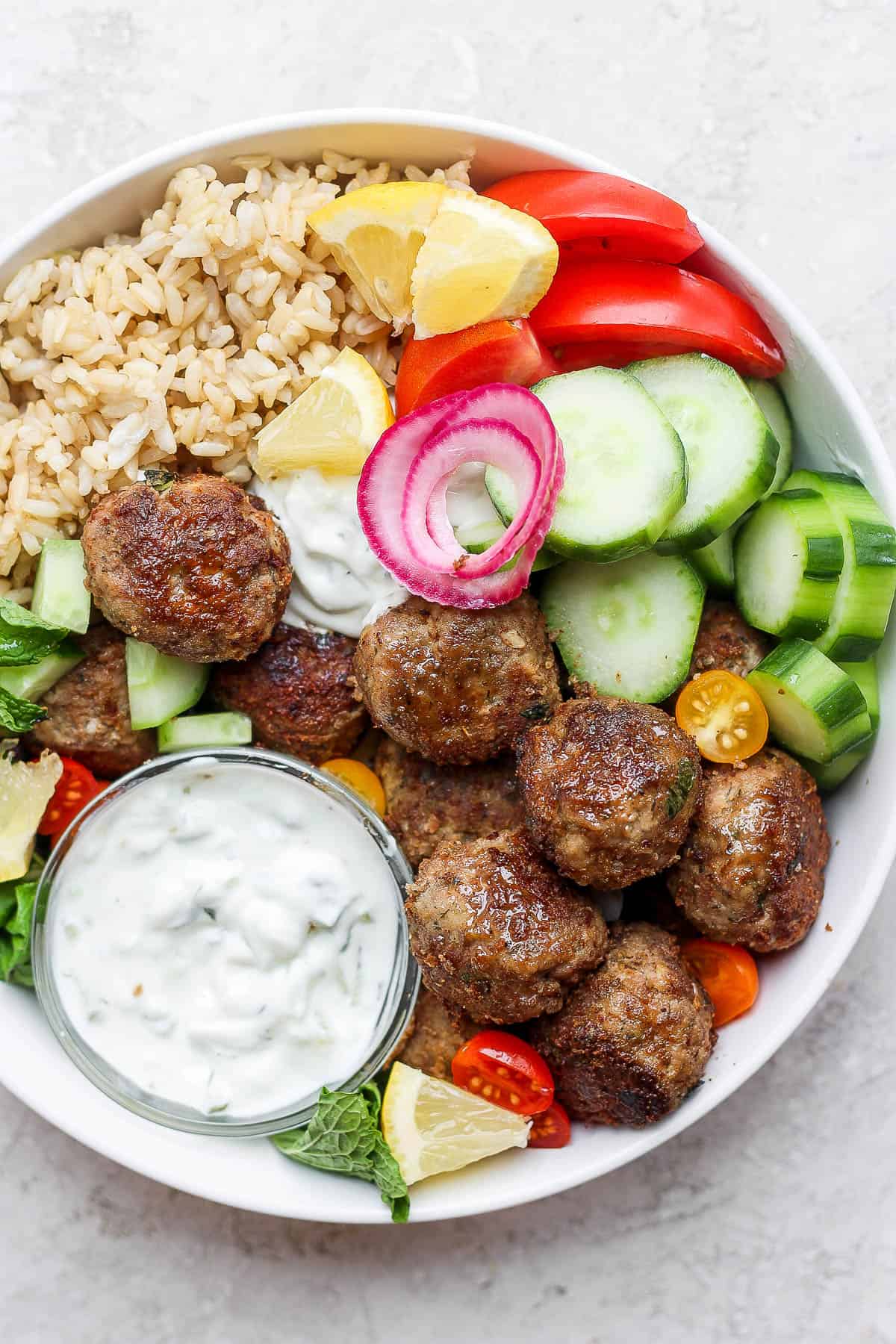 A gyro bowl with lamb meatballs, tzatziki sauce, tomatoes and cucumbers. 