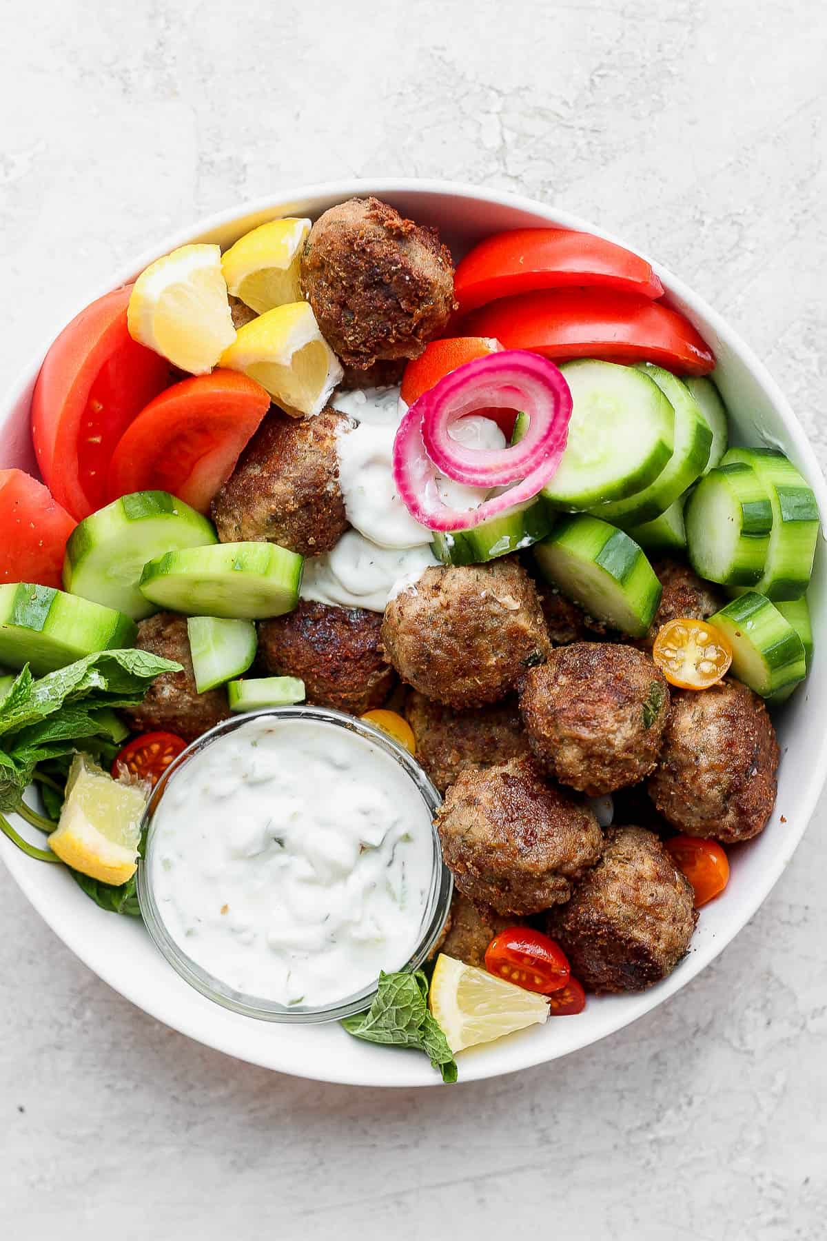 A gyro bowl with lamb meatballs, tzatziki sauce, tomatoes and cucumbers. 