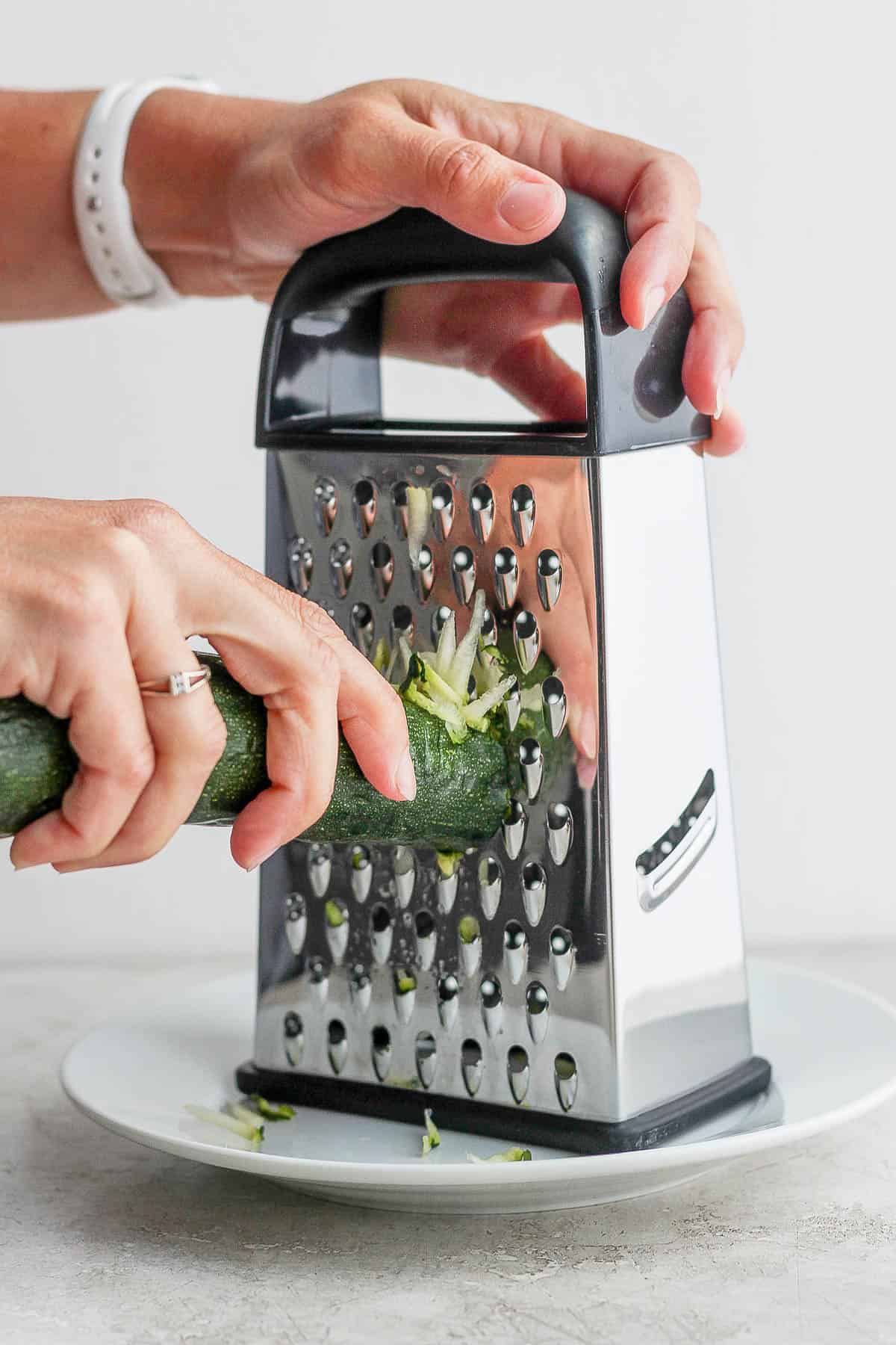 Someone grating zucchini with a box grater.