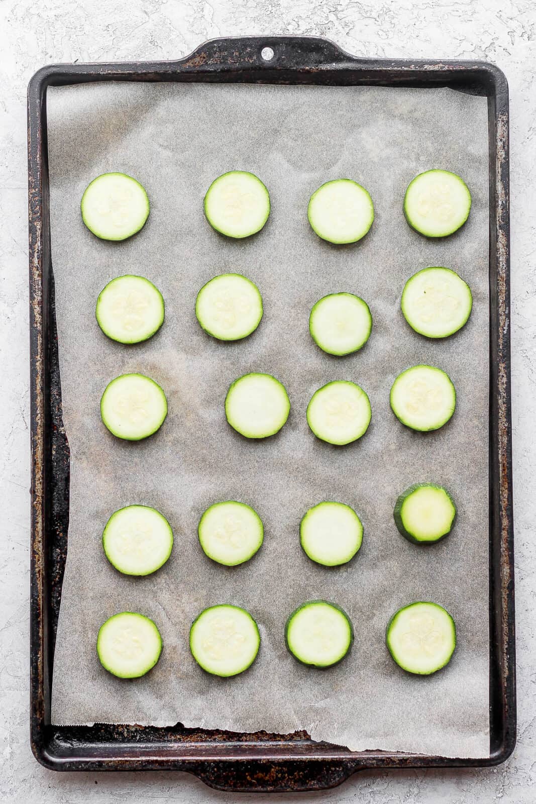 Blanches slices of zucchini on a parchment-lined baking sheet.