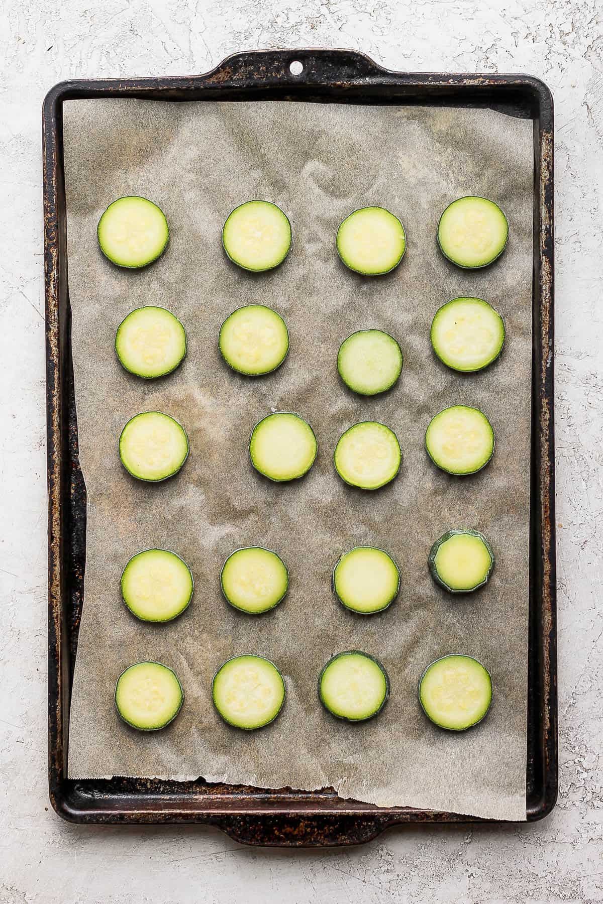 Frozen slices of zucchini on a parchment linked baking sheet.