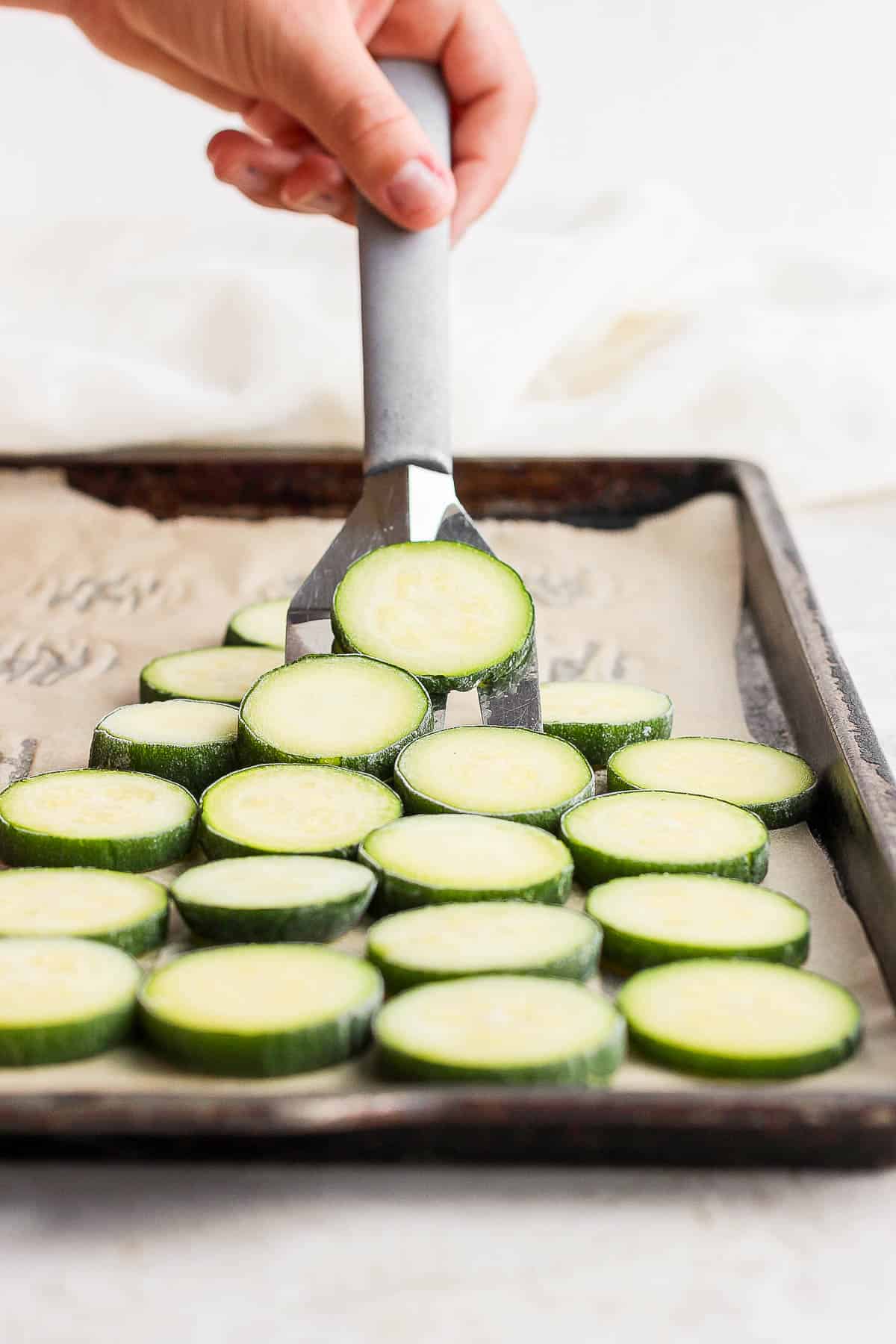 Someone scooping up frozen zucchini slices with a spatula. 