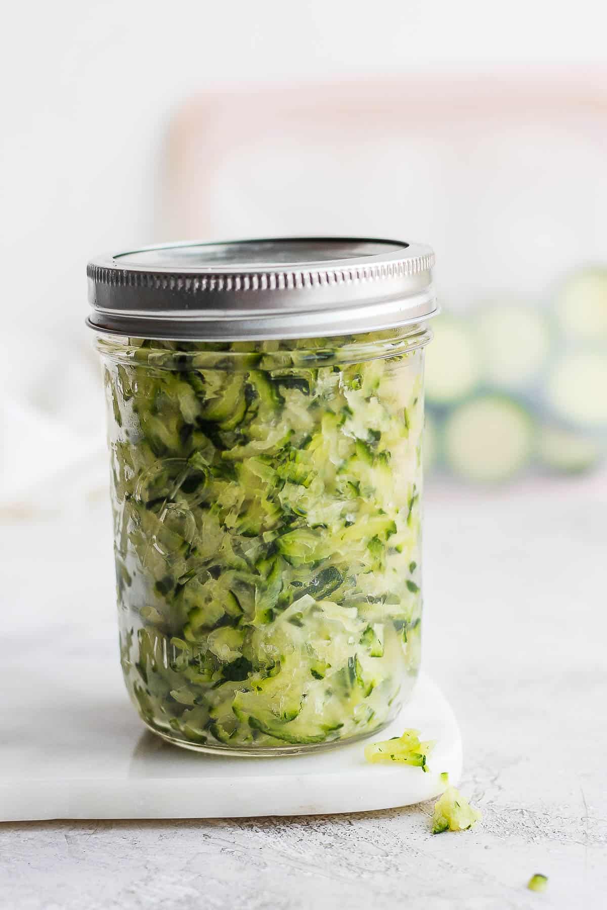 A mason jar filled with grated zucchini to be frozen.