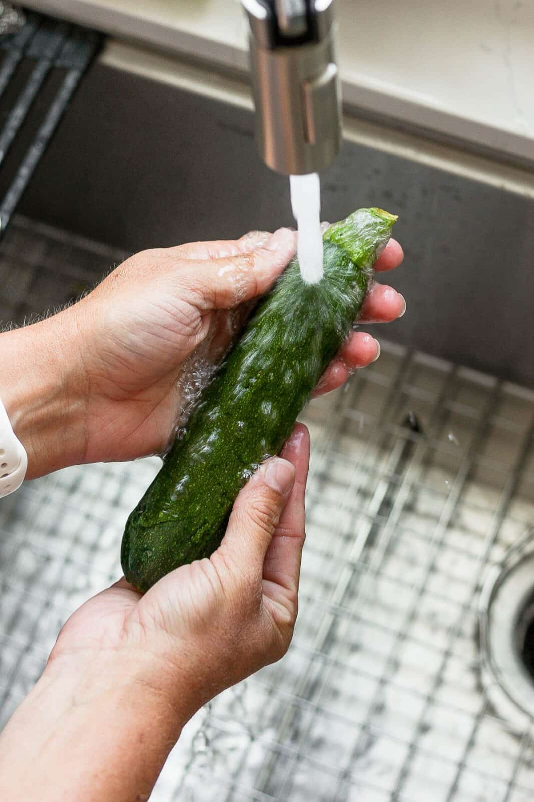 Someone washing off a zucchini in the sink.
