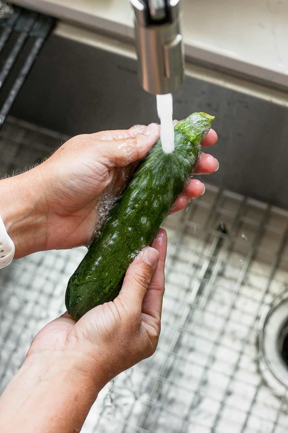 Someone washing off a zucchini in the sink. 