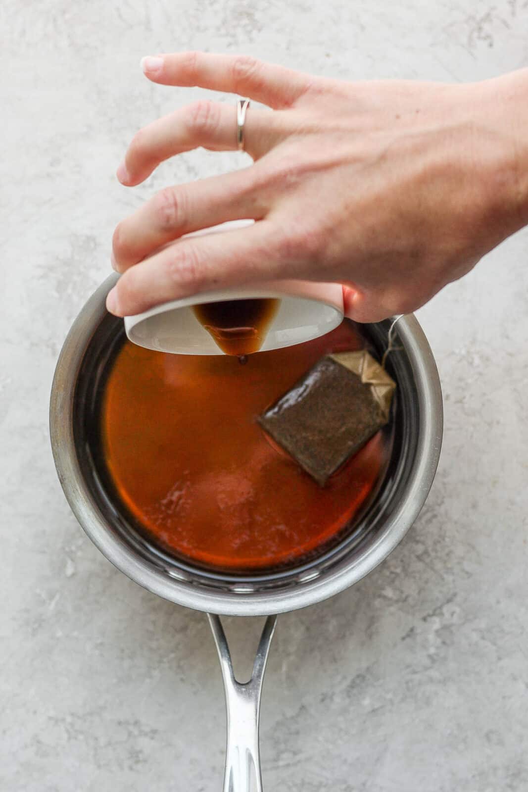 Adding maple syrup and vanilla to earl grey tea steeping in a small saucepan.