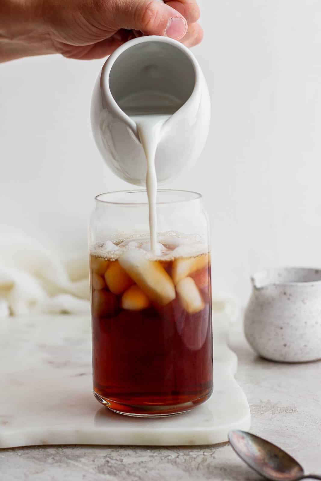 Adding almond milk to a glass of iced early grey tea.