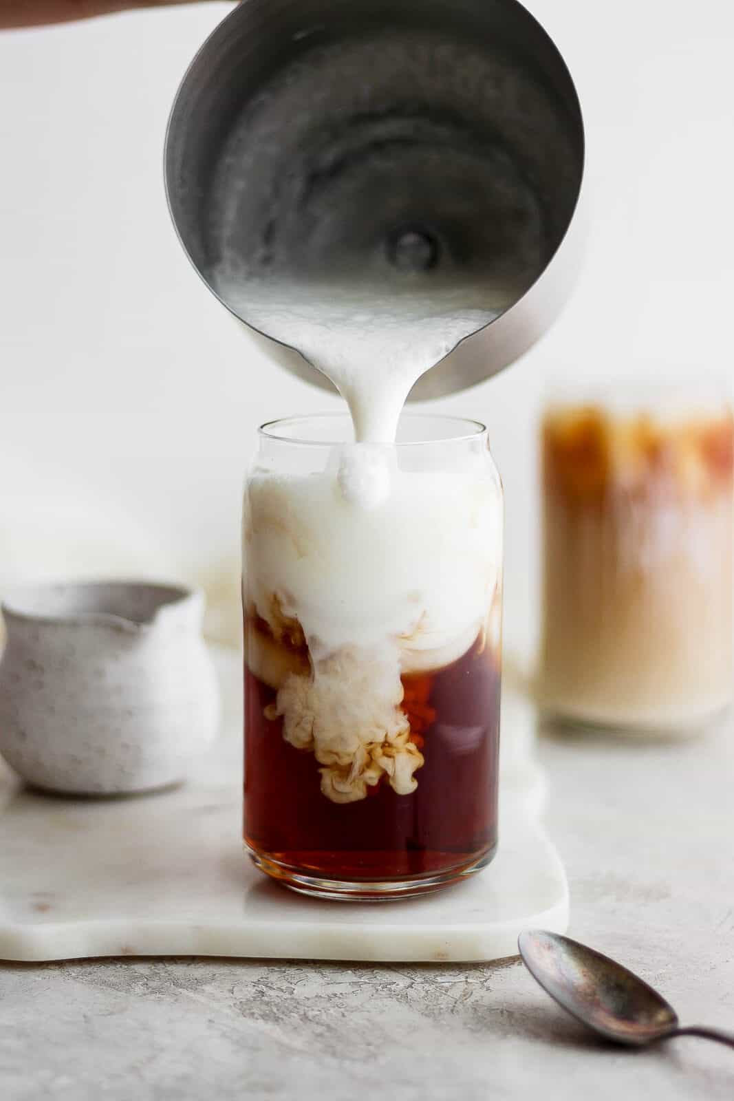 Adding frothed almond milk to a glass of iced early grey tea.