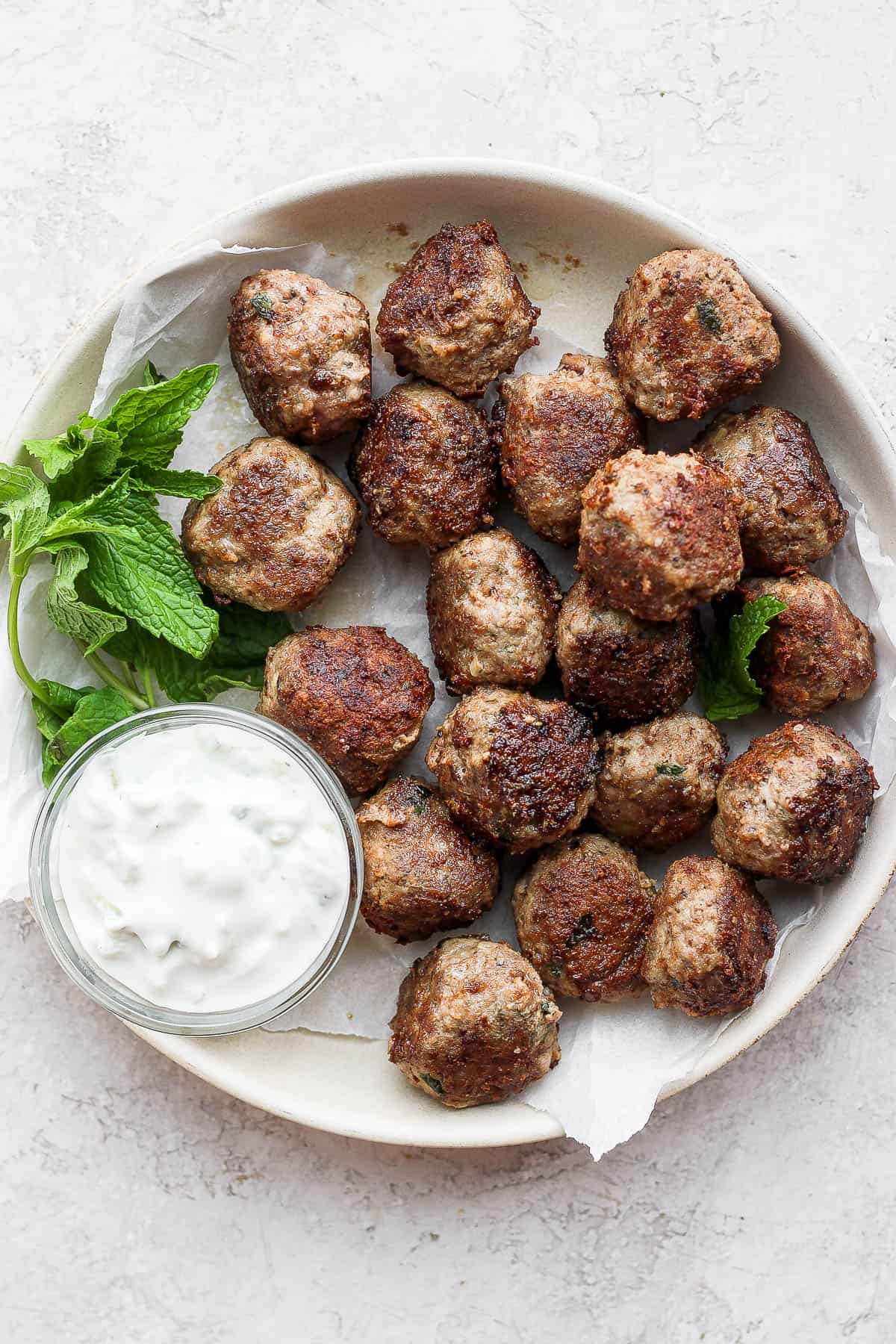 Lamb meatballs in a shallow bowl with mint and tzatziki sauce.
