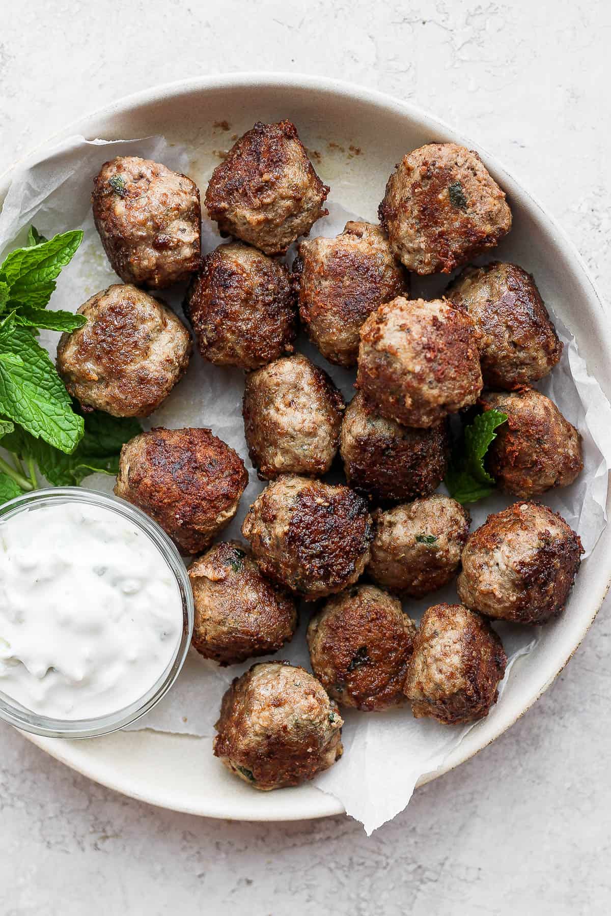 A shallow bowl of lamb meatballs with mint and tzatziki sauce.