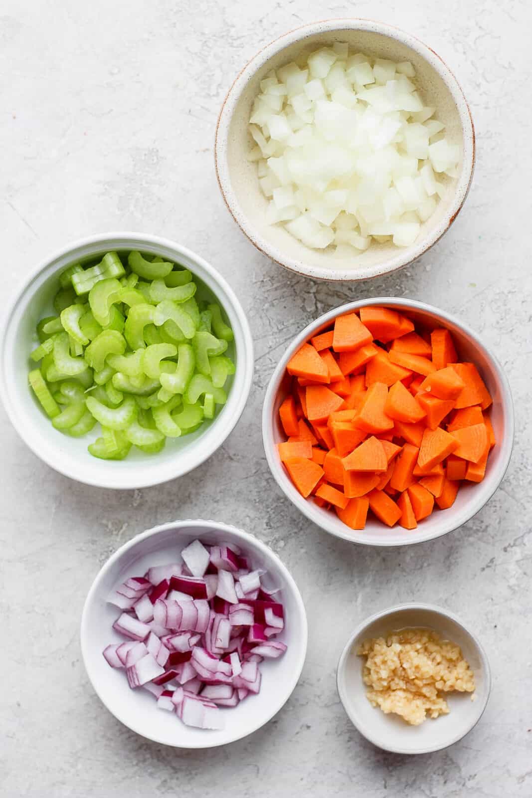 Small bowls full of celery, carrots, yellow onion and purple onion.