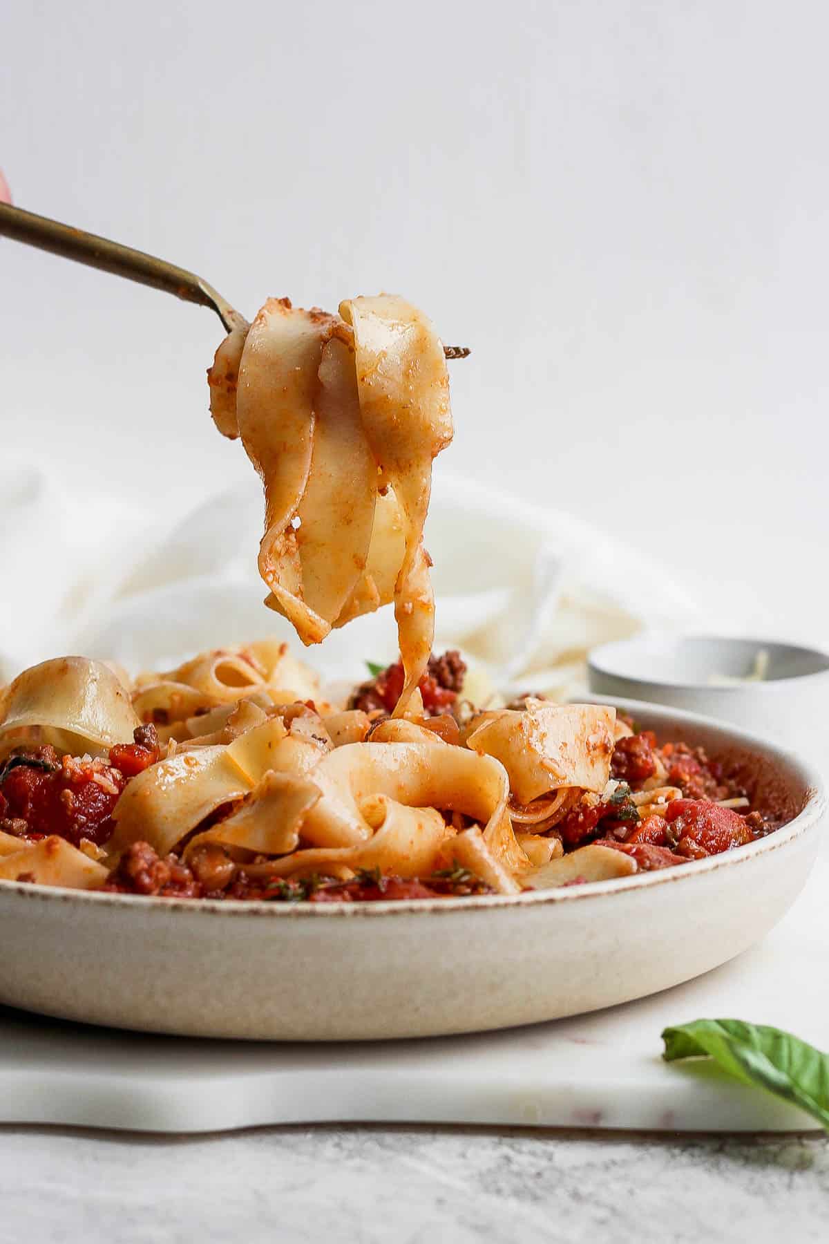 Bowl of pappardelle bolognese with someone lifting out a bunch of noodles. 