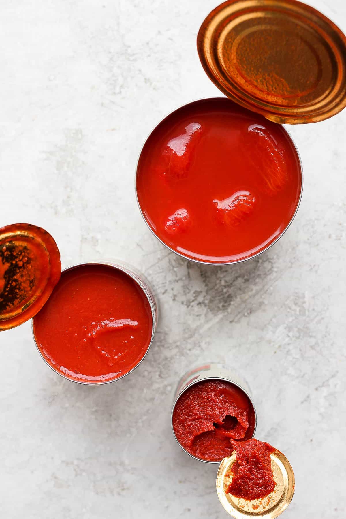 Top shot of opened cans of whole tomatoes, tomato paste and tomato sauce.