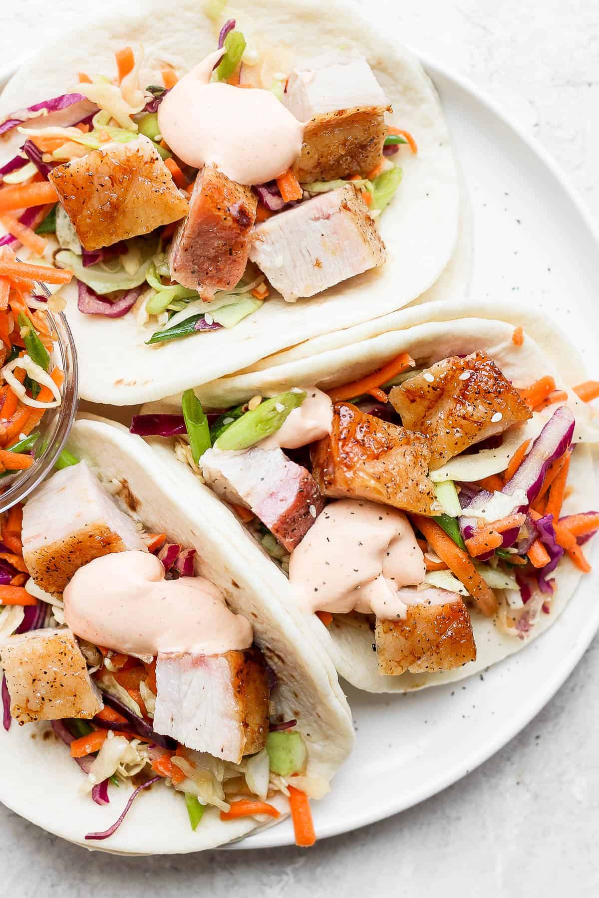 Three pork belly tacos on a plate.