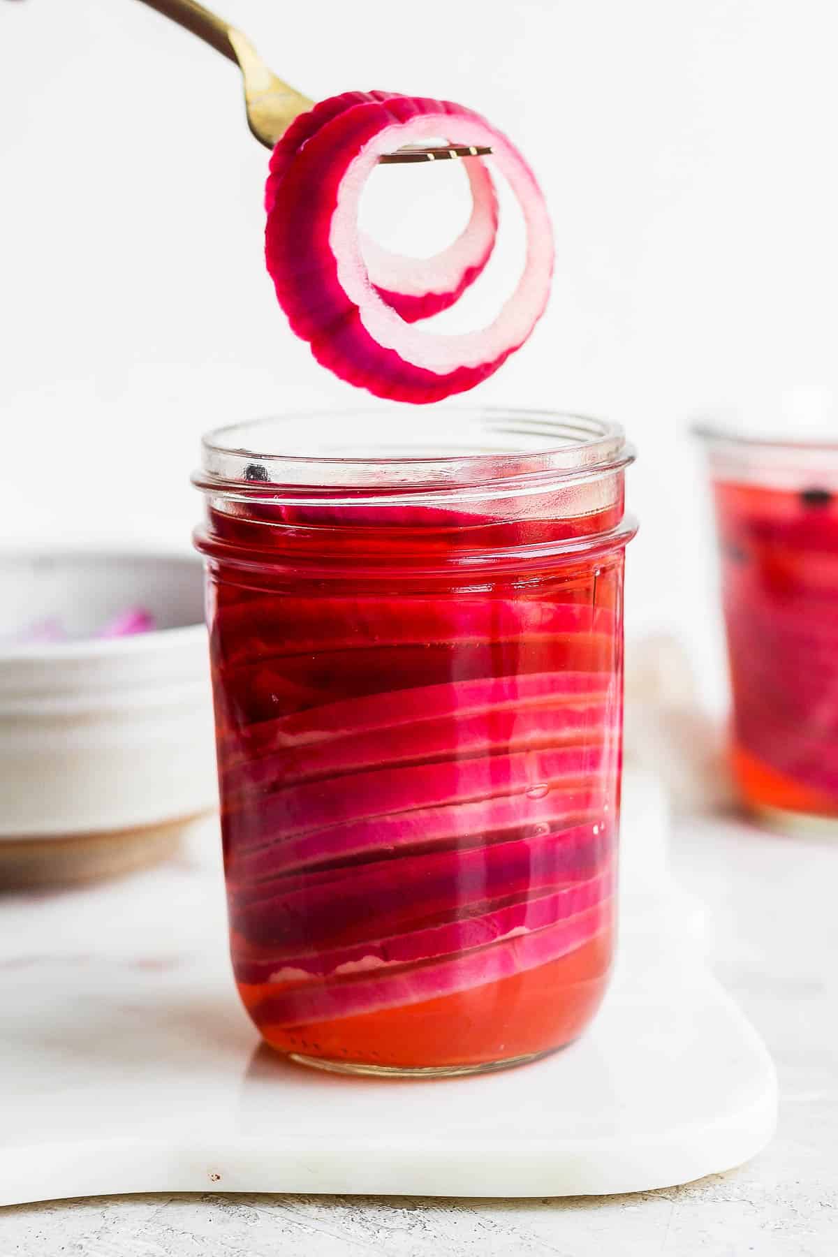 A fork scooping 2 slices of pickled onions out of the jar.