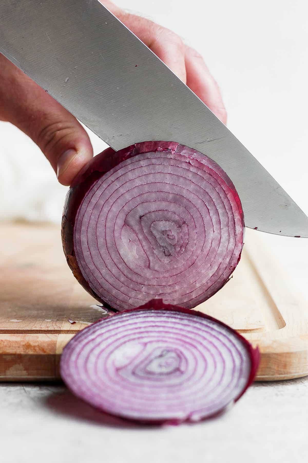 A red onion being sliced on a cutting board.