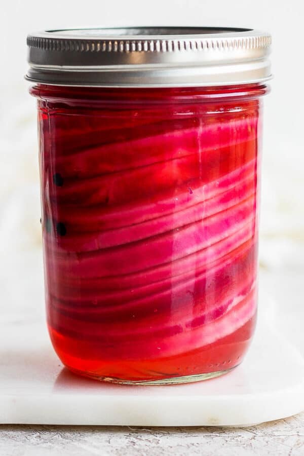 A jar of quick pickled red onions with the top on.