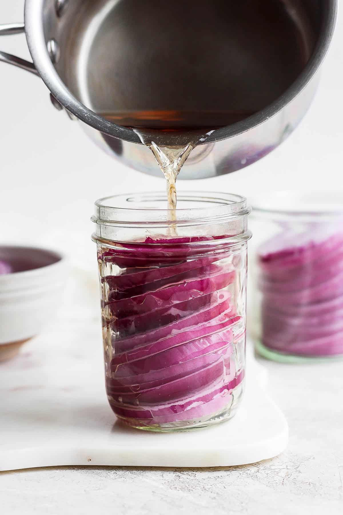 Vinegar mixture being poured from the saucepan into the jar with red onions.