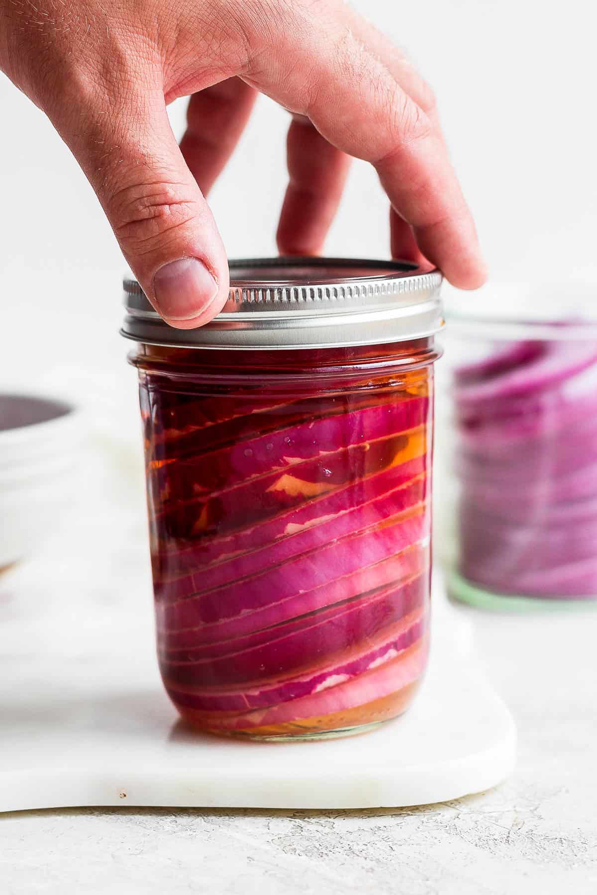 Placing a top on the jar of quick pickled onions.