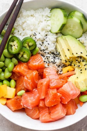 Top down shot of a salmon poke bowl with avocado, mango, cucumber and edamame.