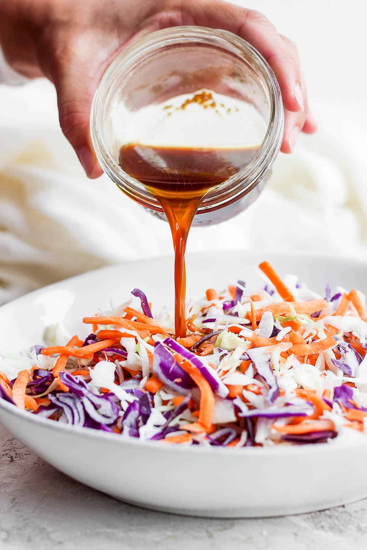 The sauce being poured from a mason jar onto the slaw ingredients.
