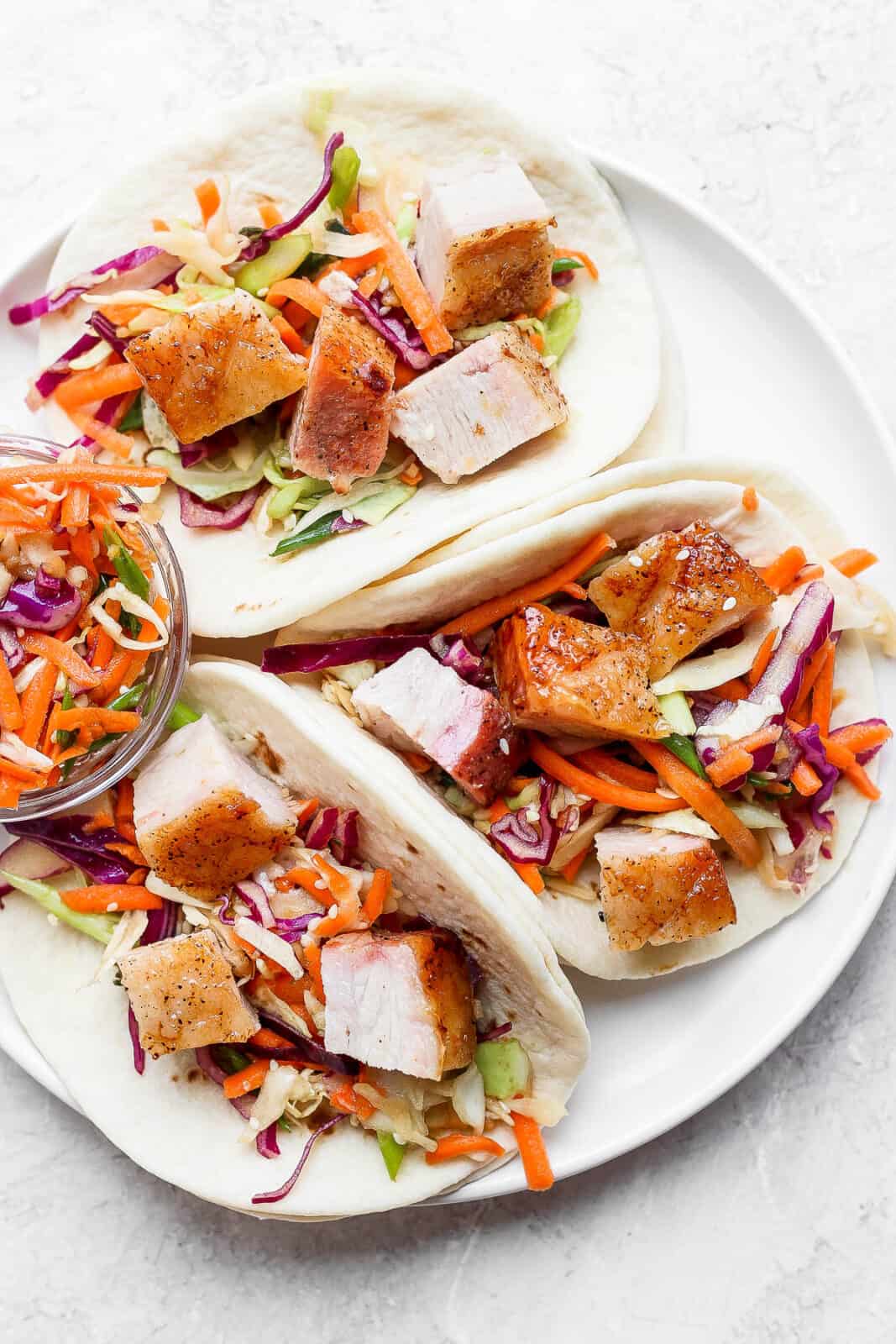 Three pork belly tacos with sesame ginger slaw on a plate.