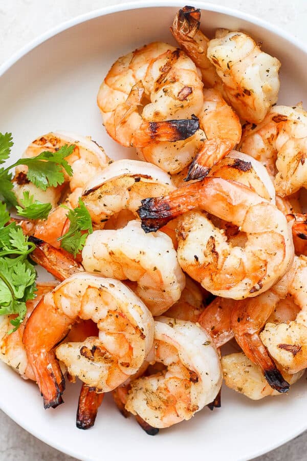 Several cooked, marinated shrimp in a white bowl.