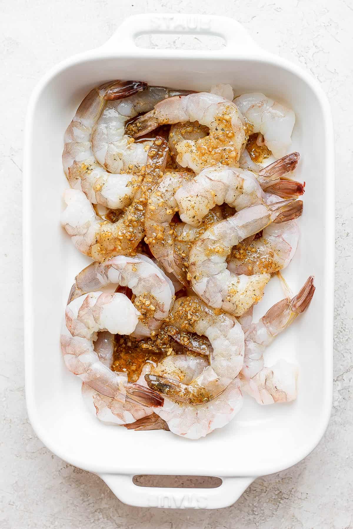 Raw shrimp in a dish with marinade on top.