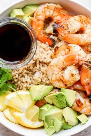 A bowl of shrimp, brown rice, avocado and soy sauce.