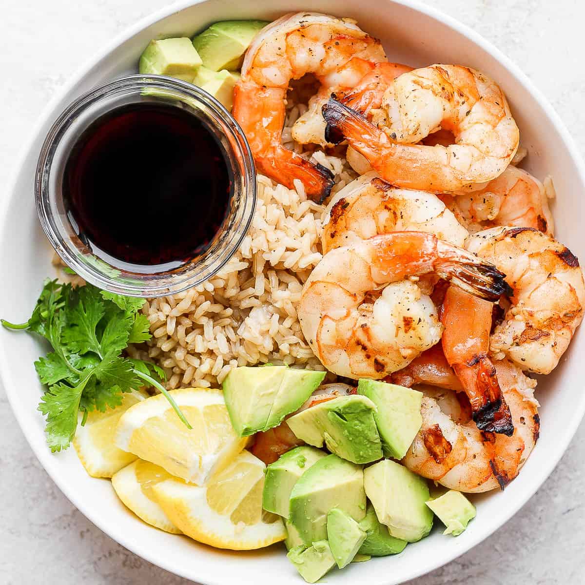 A bowl of shrimp, brown rice, avocado and soy sauce.