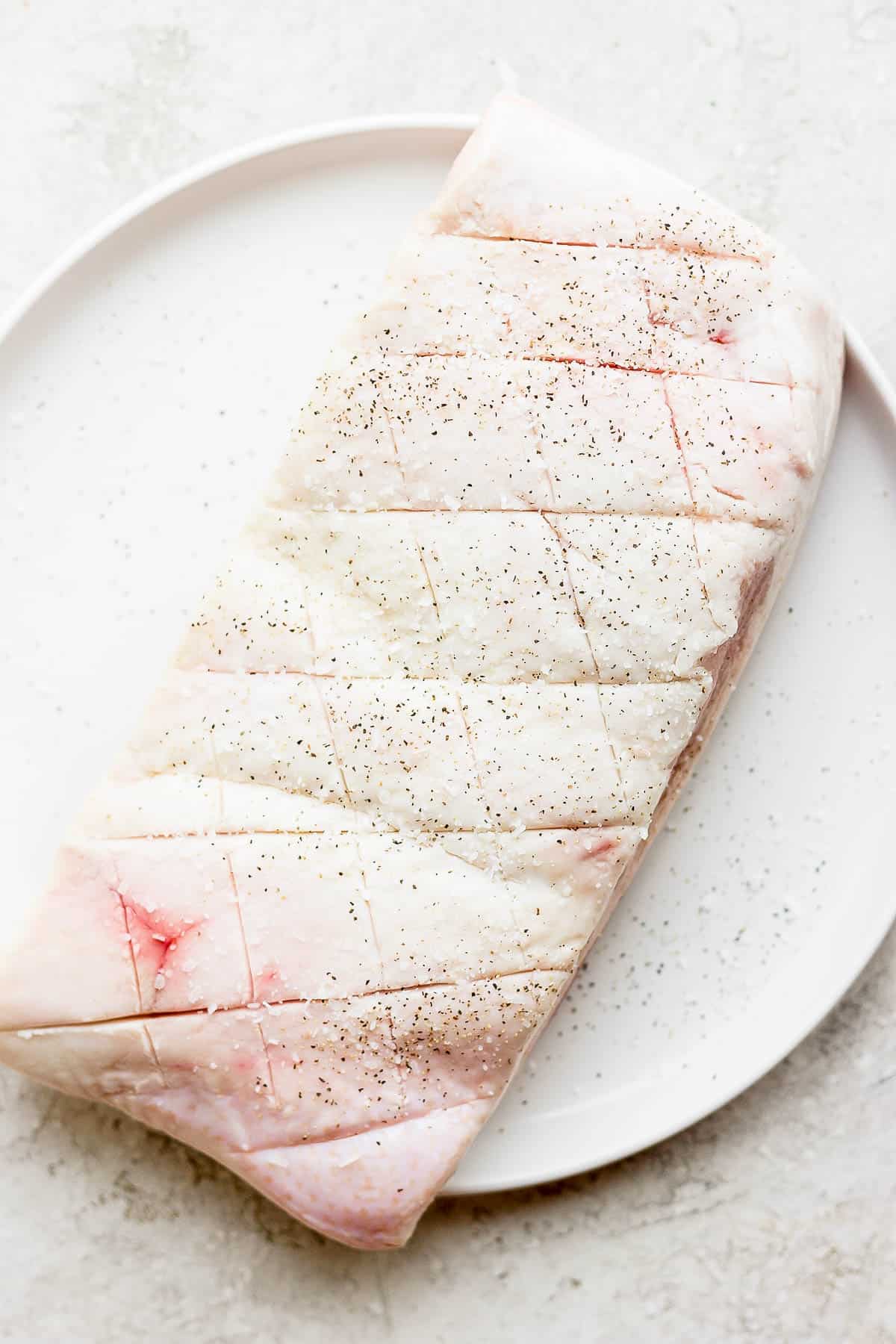 A slab of pork belly on a plate, seasoned and scored.