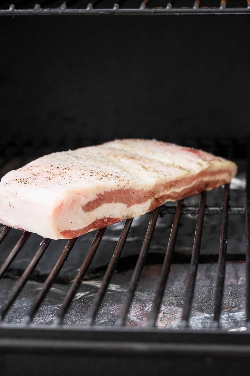 A slab of pork belly on a smoker.
