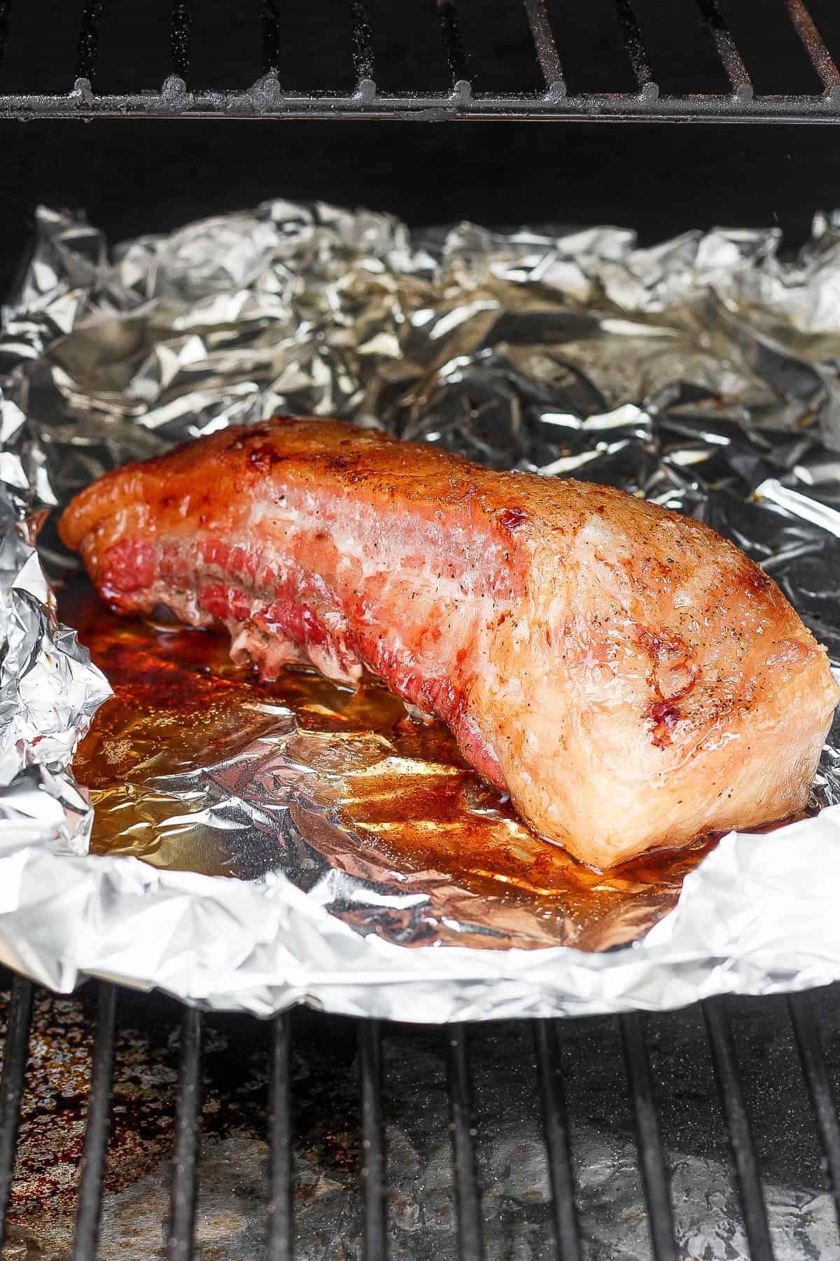 A slab of pork belly sitting in some tin foil on the smoker.