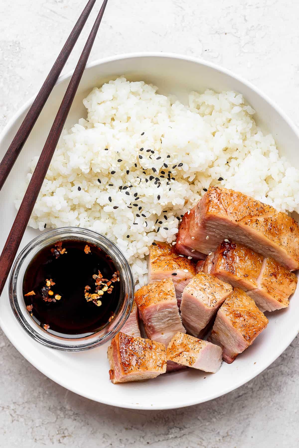 A bowl of rice, soy sauce and pork belly. 