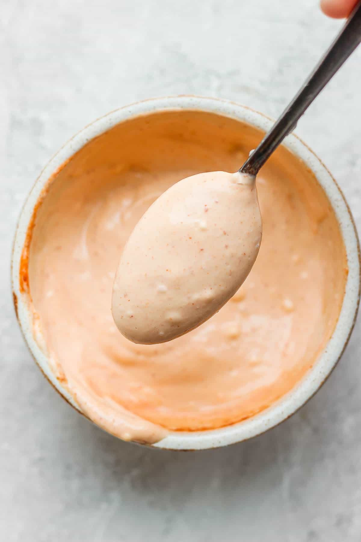 Bowl of spicy mayo with someone raising a spoon of it up towards the camera.