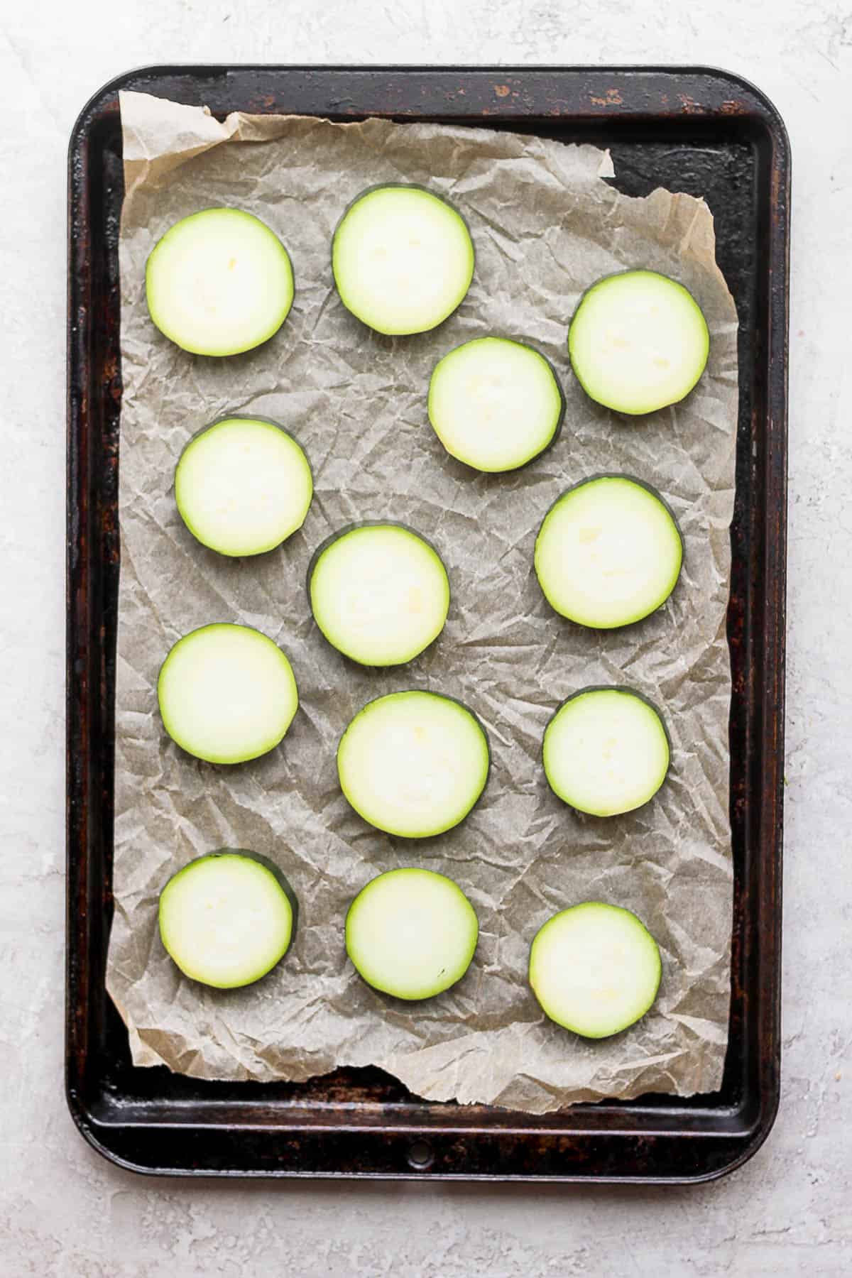Slices of zucchini on a parchment-lined baking sheet.