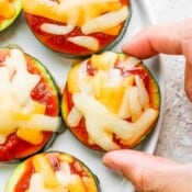 Top down shot of a plate of zucchini pizza bites with someone grabbing one off of the plate.