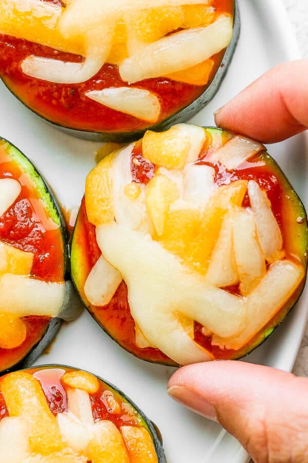 Top down shot of a plate of zucchini pizza bites with someone grabbing one off of the plate.