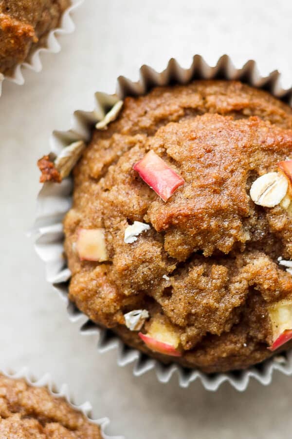An apple cinnamon muffin with two other muffins next to it.